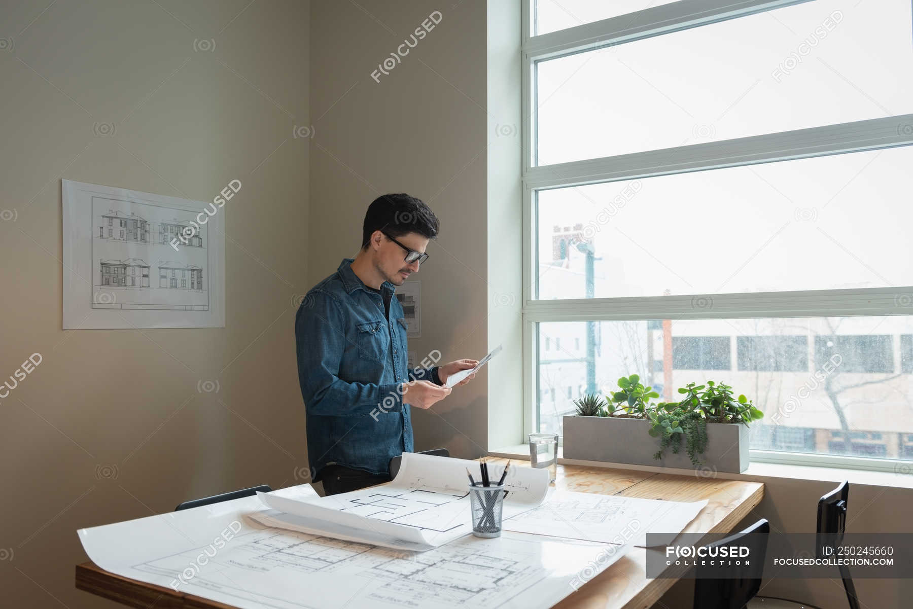 Side View Of Businessman Standing And Looking Blueprint At