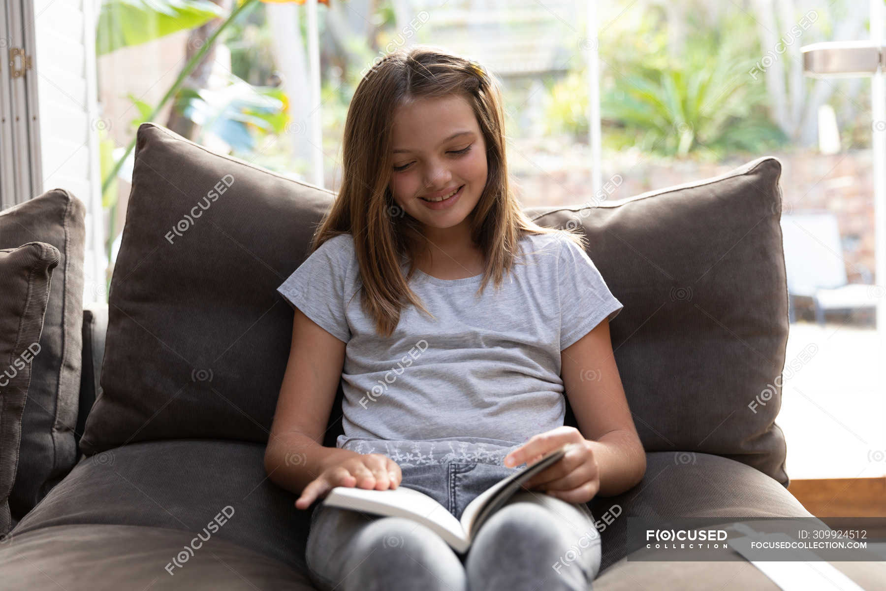 Front view of a smiling tween Caucasian girl sitting on a comfortable chair reading in her