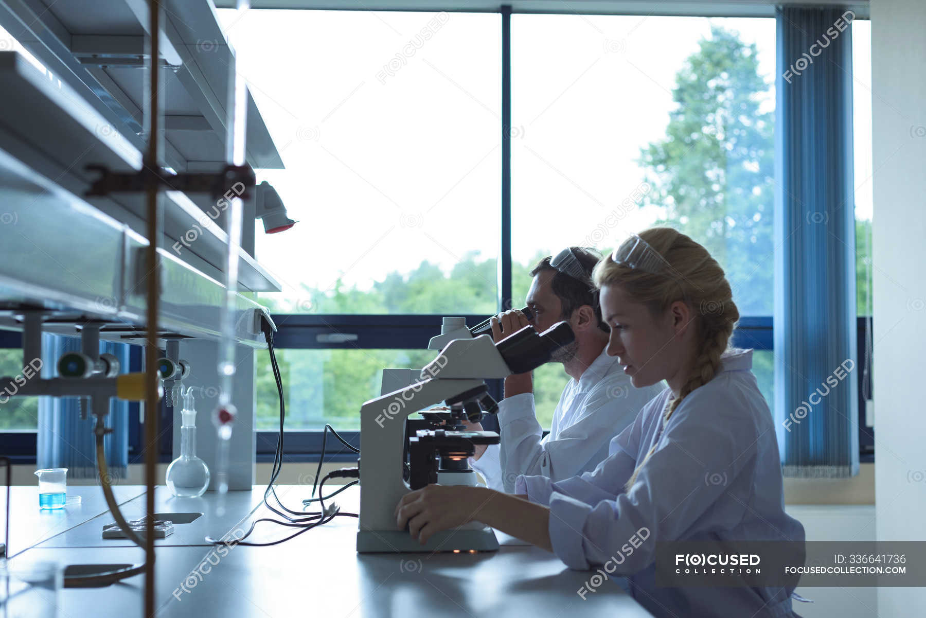 University students doing experiment on microscope in laboratory at college — Mature Adult