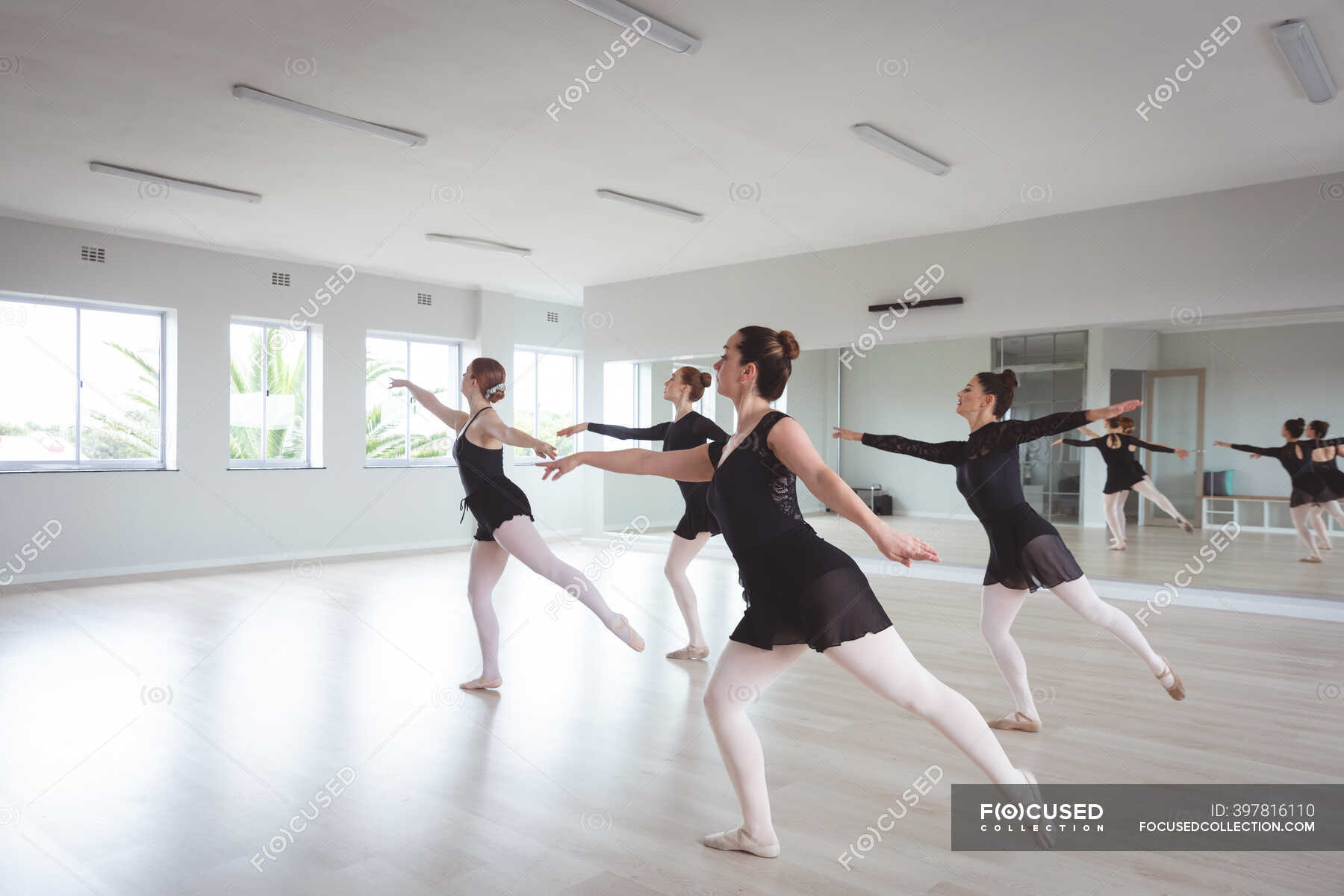 A group of Caucasian female attractive ballet dancers in black outfits  practicing during a ballet class in a bright studio, dancing in unison in  front of a mirror. — elegance, friends -