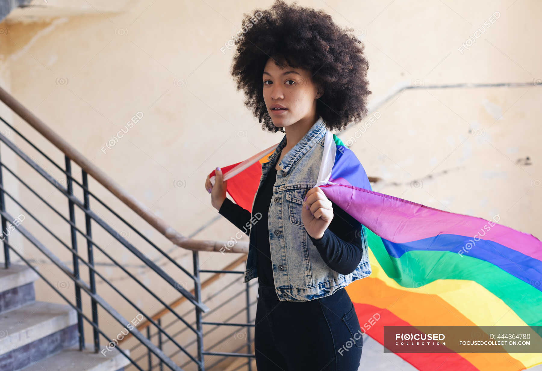 Mixed race woman holding a rainbow flag looking at camera. gender fluid ...