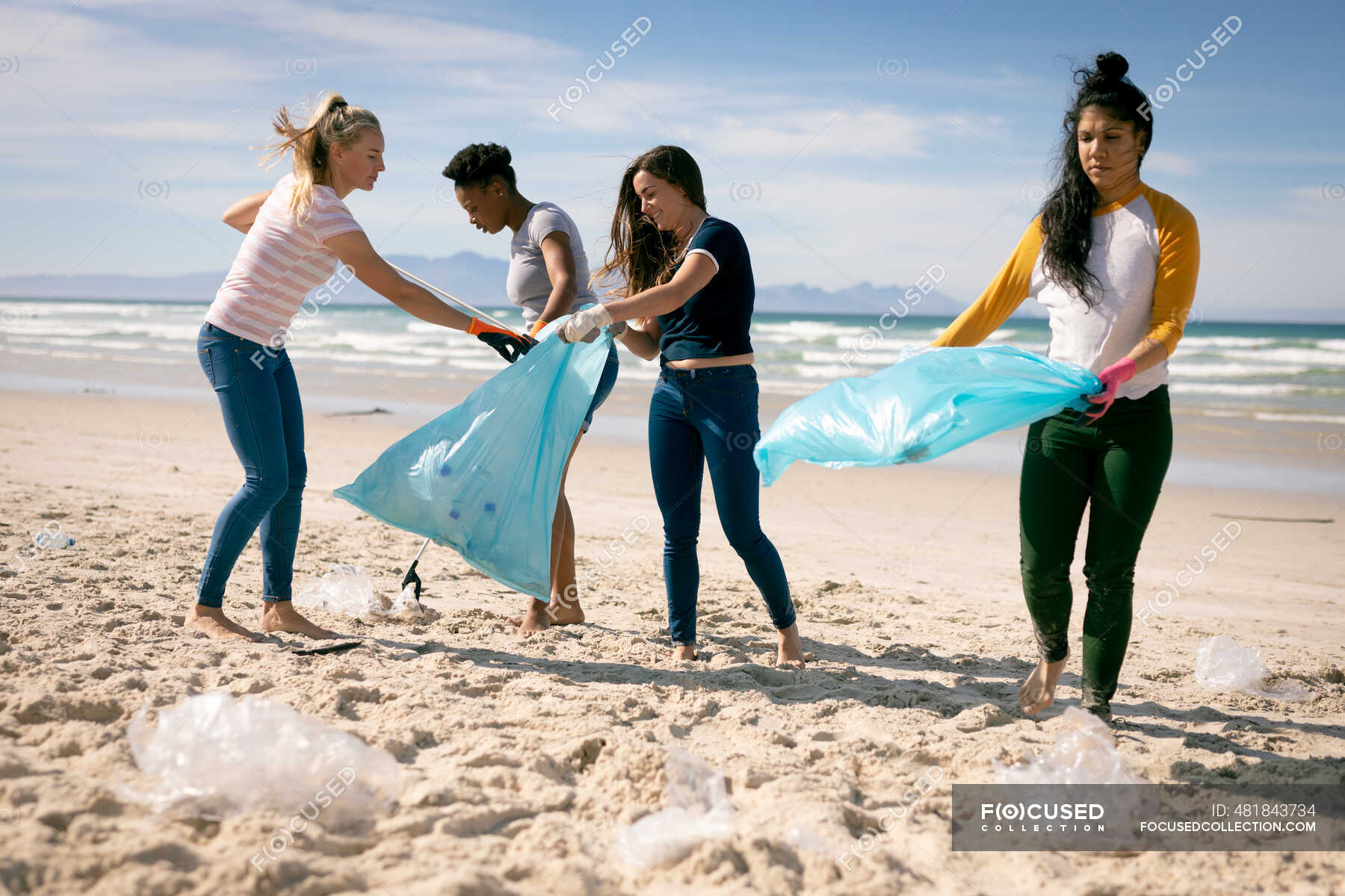 Diverse group of women walking along beach, picking up plastic rubbish ...