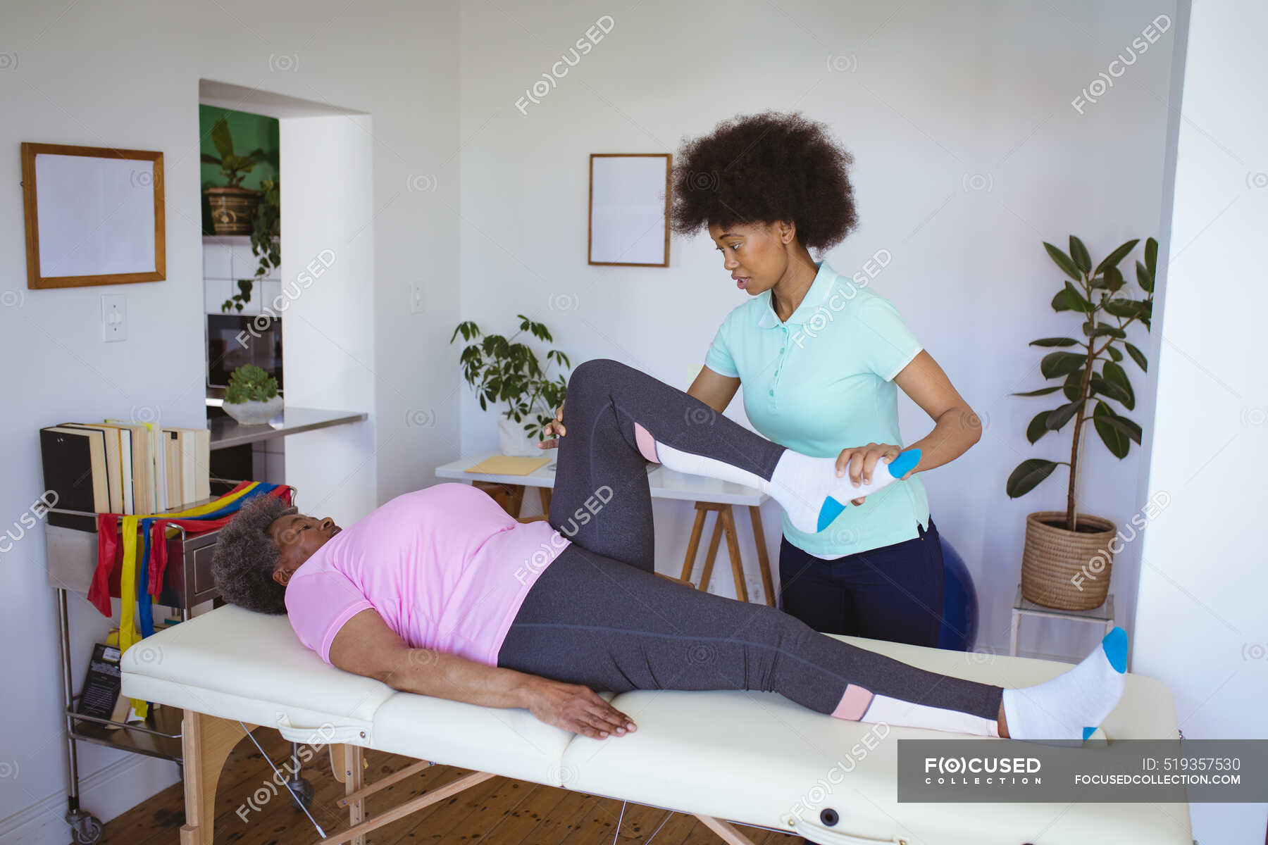 African american female physiotherapist treating leg of senior female