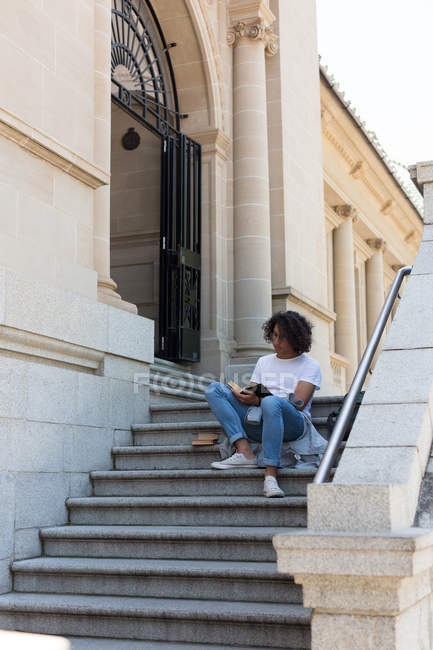 Молодой человек, читающий книгу у здания библиотеки — стоковое фото