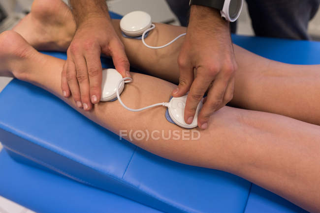 Physiotherapist placing pads on woman legs in clinic — Stock Photo