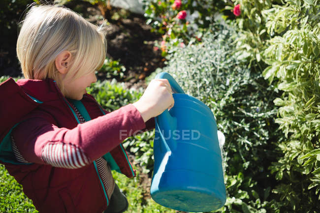 Хлопчик поливає рослини в саду в сонячний день — стокове фото