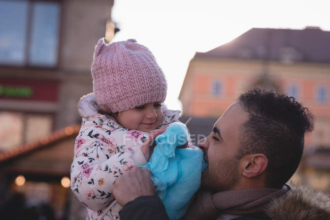Pai e filha tendo algodão doce ao entardecer no parque de diversões — Fotografia de Stock