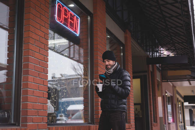 Young man using mobile phone outside the shop — Stock Photo