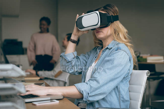 Исполнительный директор работает на ноутбуке, используя гарнитуру виртуальной реальности в офисе — стоковое фото