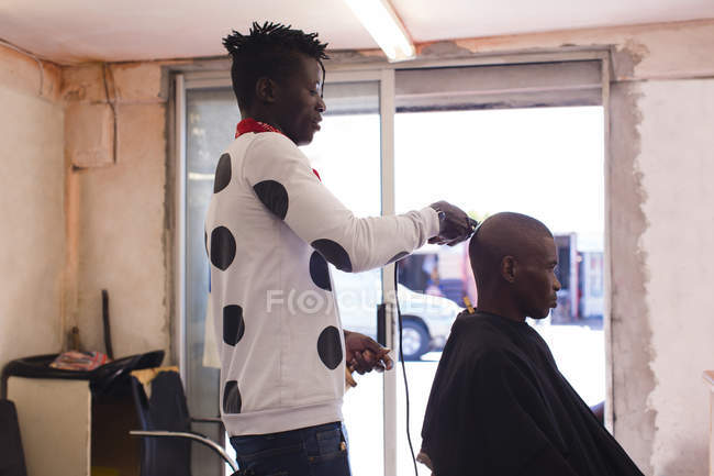 Barbeiro aparar o cabelo do cliente na barbearia — Fotografia de Stock