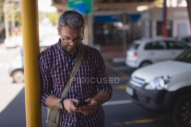 Concéntrese hombre usando el teléfono móvil mientras se apoya en el poste - foto de stock