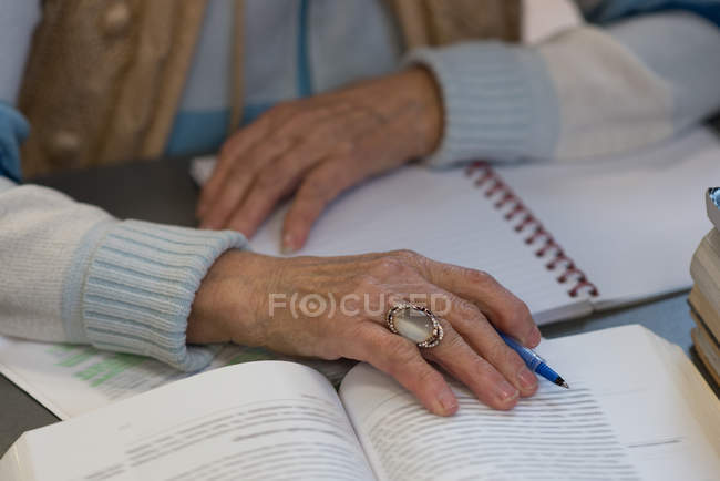 Крупним планом старша жінка, що пише в блокноті в бібліотеці — стокове фото