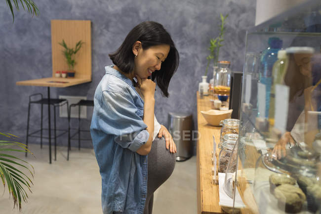 Беременная деловая женщина смотрит на сладкую еду в кафетерии в офисе — стоковое фото