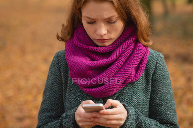 Mujer usando teléfono móvil en el parque durante el otoño - foto de stock
