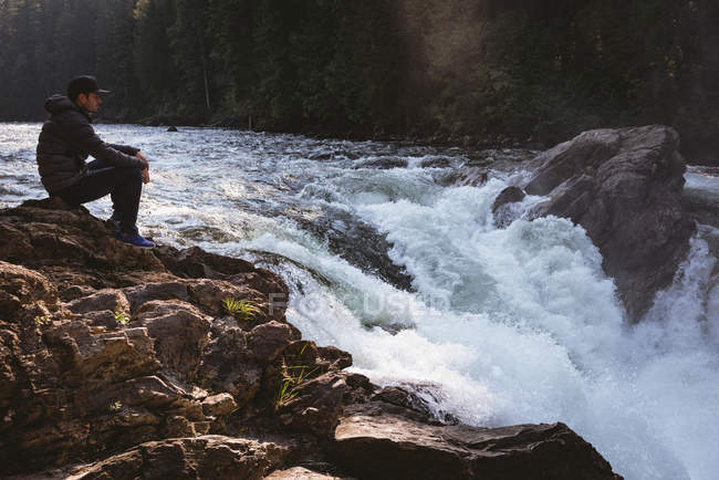 Uomo seduto sulla roccia vicino alla cascata in una giornata di sole — Foto stock