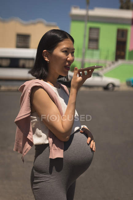Mujer embarazada tocándose el vientre mientras habla por teléfono móvil - foto de stock