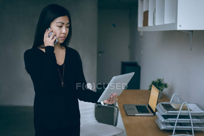 Femme cadre parlant sur téléphone portable tout en tenant tablette numérique dans le bureau — Photo de stock