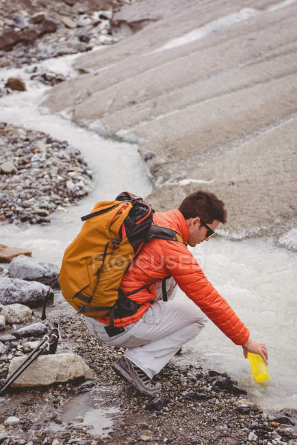 Vista lateral del agua de llenado del caminante masculino en botella del arroyo - foto de stock