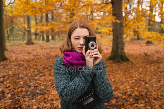Женщина фотографируется с винтажной камерой в парке осенью — стоковое фото