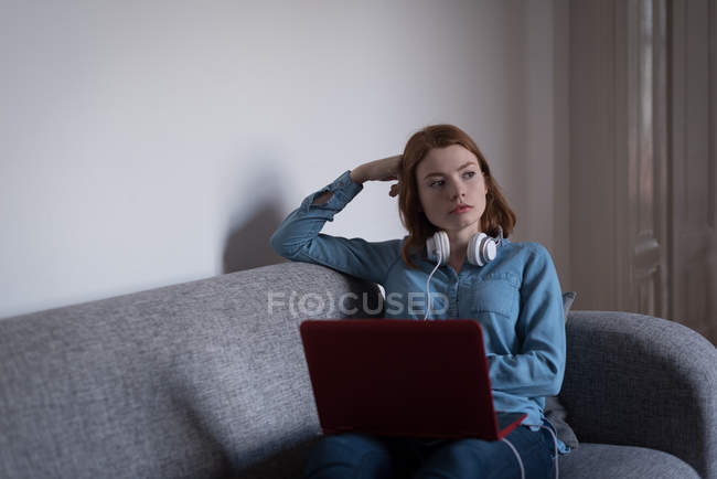 Donna premurosa con computer portatile seduto sul divano in soggiorno a casa — Foto stock
