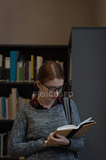 Jovem mulher lendo um livro na biblioteca — Fotografia de Stock