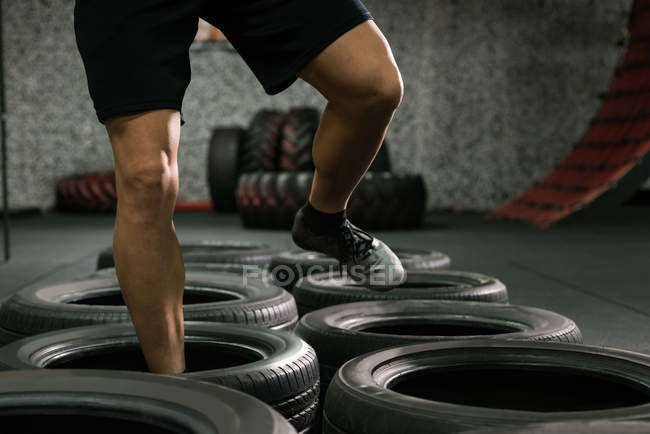 Низкая часть мускулистого человека на тренировках по прыжкам с шин в спортзале — стоковое фото