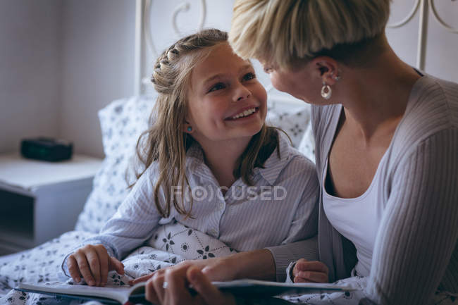 Mother and daughter interacting with each other while reading book in bedroom — Stock Photo