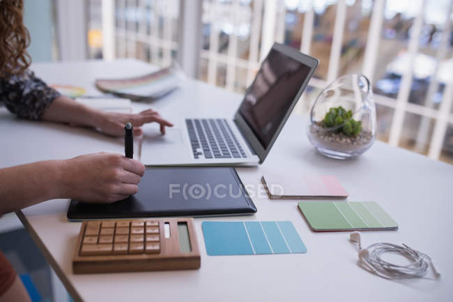 Diseñadora gráfica femenina usando tableta gráfica en el escritorio en la oficina - foto de stock