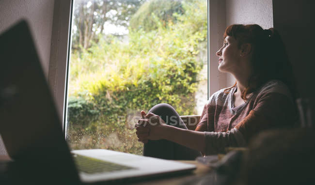 Femme réfléchie assise près de la fenêtre à la maison — Photo de stock
