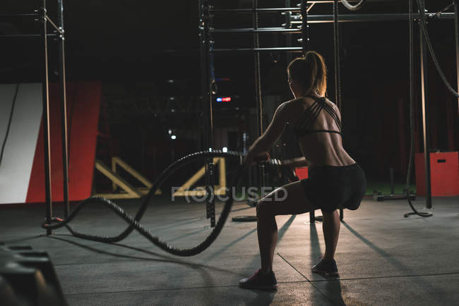 Rear view of muscular woman exercising with battle rope — Stock Photo