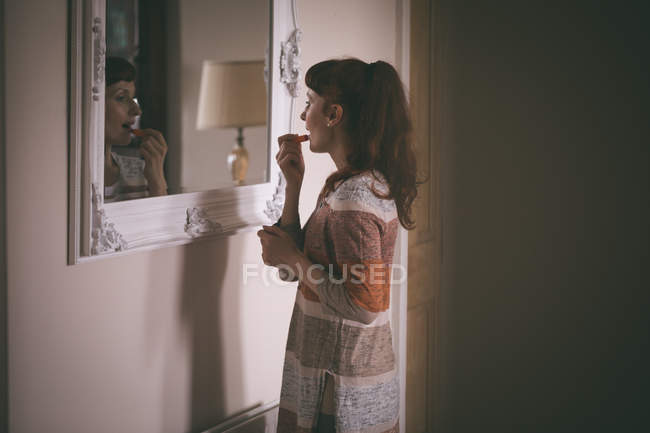 Mulher aplicando batom na frente do espelho em casa — Fotografia de Stock