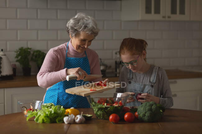 Grand-mère et petite-fille coupant des légumes dans la cuisine à la maison — Photo de stock