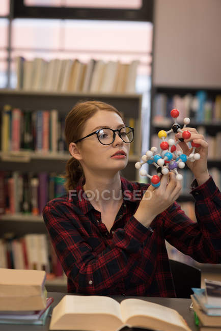 Jovem analisando um modelo de molécula na biblioteca — Fotografia de Stock