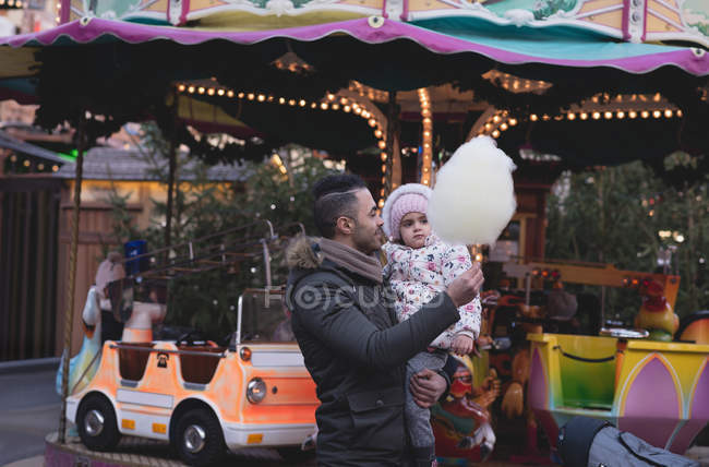 Батько і дочка мають бавовняні цукерки в сутінках в парку розваг — стокове фото
