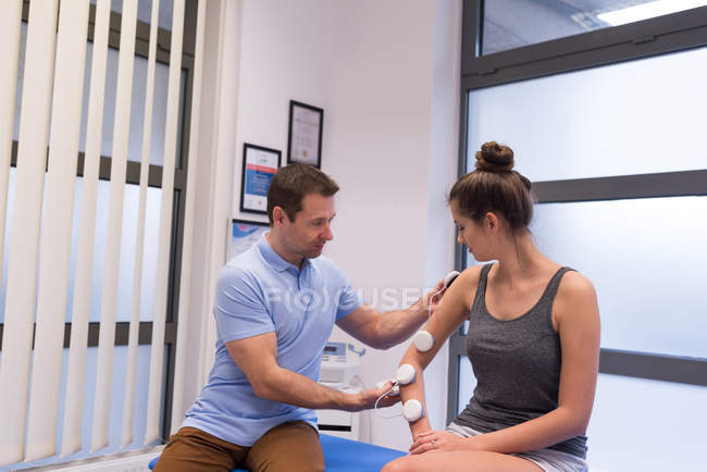 Physiotherapist applying electrode pads on woman's hand in clinic — Stock Photo