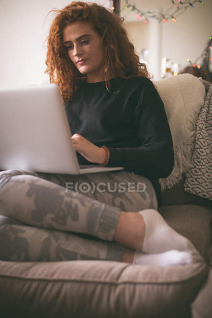 Donna che utilizza il computer portatile mentre seduto sul divano in soggiorno — Foto stock