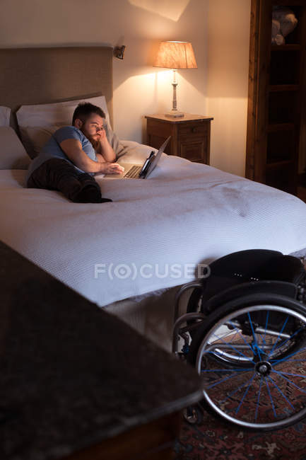 Disabled man using laptop in bedroom at home — Stock Photo