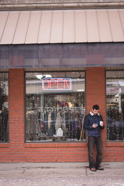 Young man using mobile phone outside the shop — Stock Photo