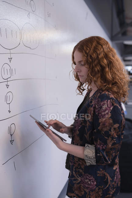 Femme exécutive utilisant tablette numérique près du tableau blanc dans le bureau — Photo de stock