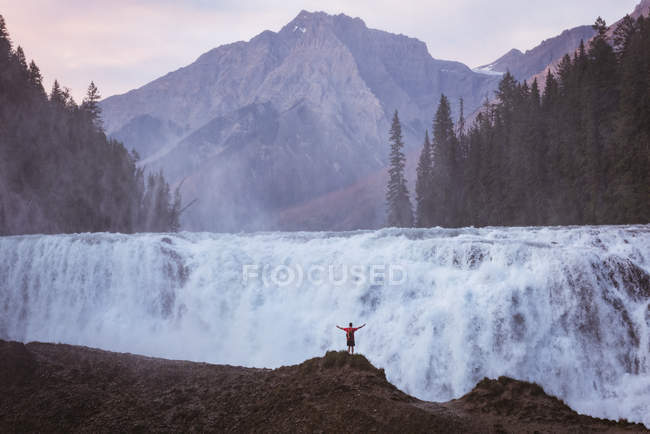 Vue arrière de l'homme debout avec les bras tendus près de la cascade — Photo de stock