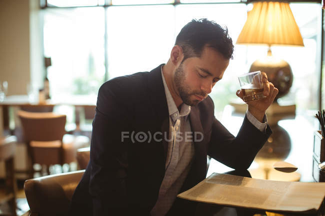 Empresario leyendo el periódico mientras toma un vaso de whisky en el hotel - foto de stock