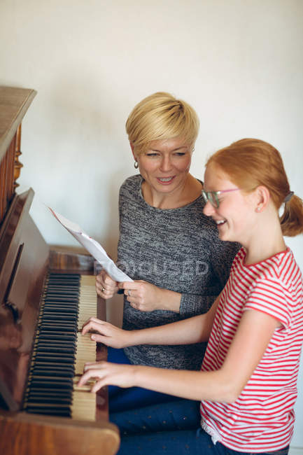Улыбающаяся мать помогает дочери играть на пианино дома — стоковое фото