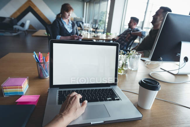 Бизнесмен использует ноутбук, пока коллеги обсуждают в офисе — стоковое фото