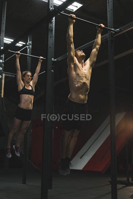 Muskulöses Paar übt das Hochziehen an einer Klimmzugstange in der Turnhalle — Stockfoto
