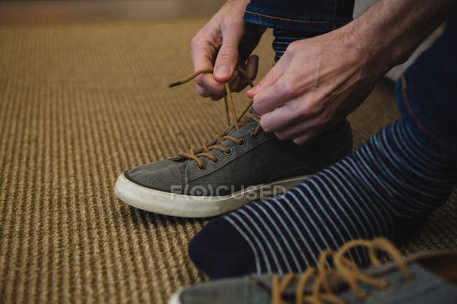 Section basse de l'homme attachant des lacets dans le salon à la maison — Photo de stock