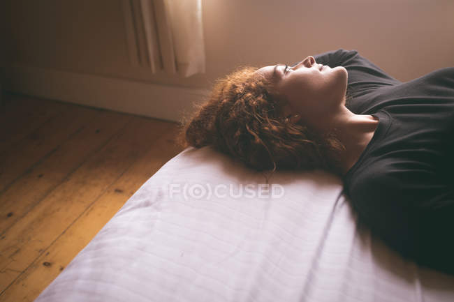 Thoughtful woman lying on bed in bedroom at home — Stock Photo