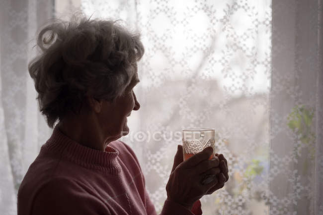Старшая женщина, стоящая у окна дома — стоковое фото