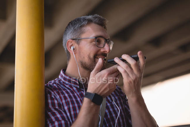 Sonriente hombre hablando en el teléfono móvil mientras se apoya en el poste - foto de stock