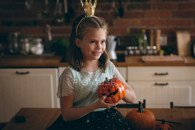 Chica sosteniendo calabaza tallada en la cocina en casa - foto de stock