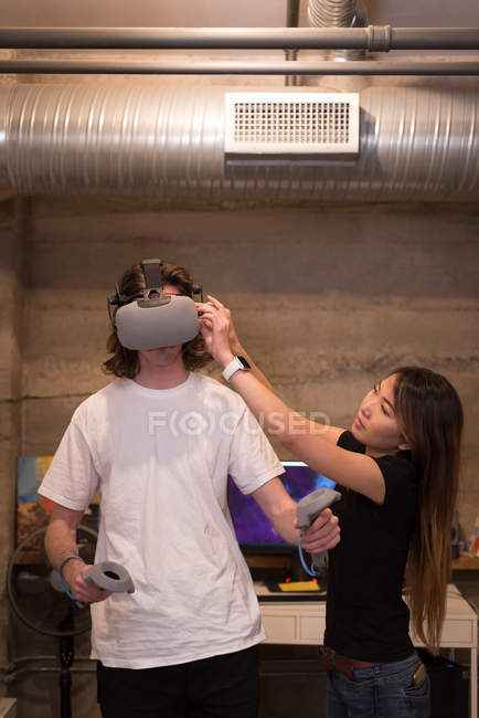 Ejecutiva femenina ayudando a ejecutivo masculino en el uso de auriculares de realidad virtual en la oficina - foto de stock